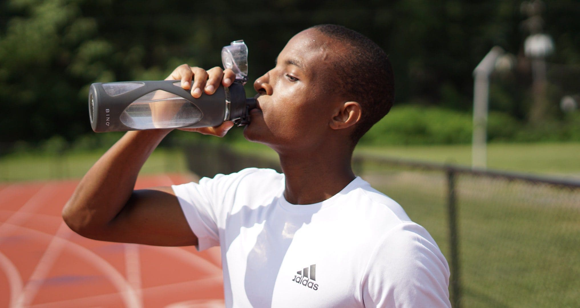 man standing on a running track drinking a refillable water bottle