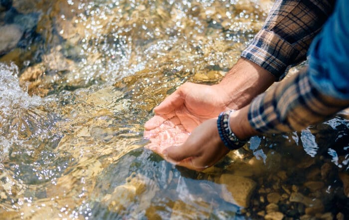 Native American man cupping water from river in his hands.