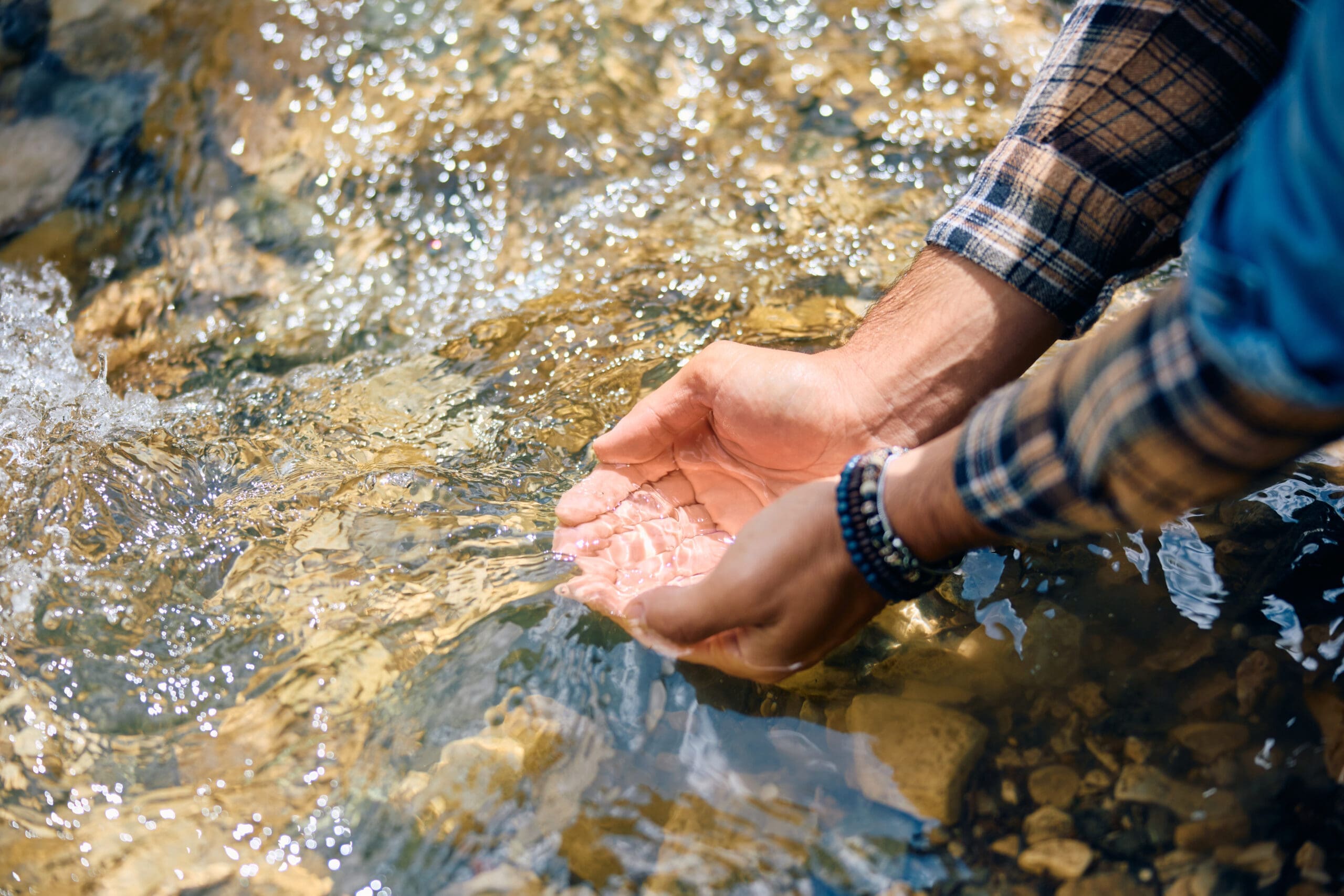 Native American man cupping water from river in his hands.