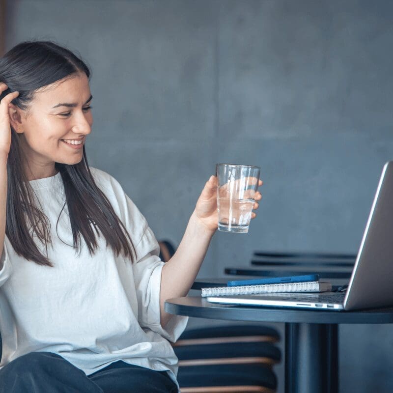 young woman drinking from glass in front of her computer